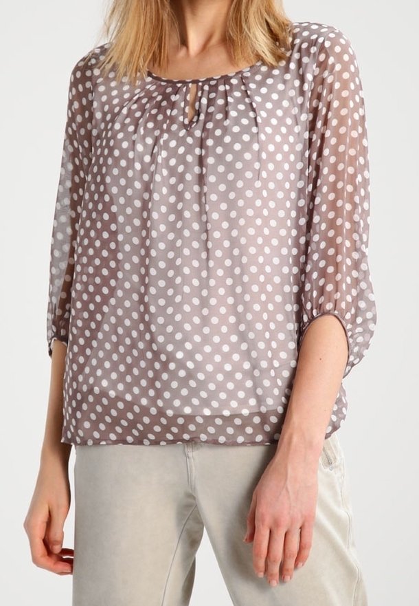Blusa leggera e trasparente color taupe con pois bianchi. Presenta una scollatura tonda, dettaglio a forma di chiave e maniche a 3/4. Texture liscia.