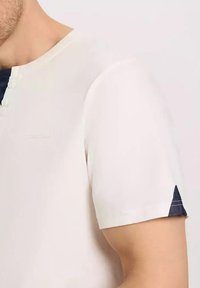 Biała koszula z krótkim rękawem z dekoltem henley, z denimu na końcach rękawów. Gładka tekstura, lekki materiał.