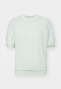 Light green sweatshirt with short sleeves, ribbed cuffs, and neckline, featuring a small embroidered logo on the chest. Soft fabric texture.