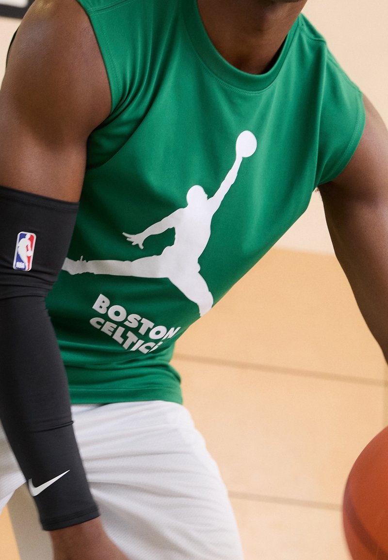 Gespiereerde basketbalspeler in een groen mouwloos shirt van de Boston Celtics en een zwarte armbeschermer, met een oranje basketbal in de hand.