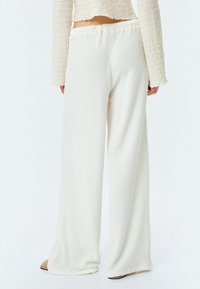 Wijdbeenbroek van gestructureerde witte stof met een elastische tailleband. Heeft een geplooid ontwerp en een lichte flair vanaf de knie.