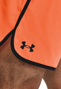 Orange idrottsshorts med svarta accenter, med en böjd nederkant och en framträdande svart Under Armour-logotyp på den nedre vänstra sidan.