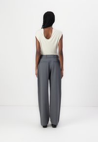 Haut beige clair avec un dos creusé, associé à un pantalon gris taille haute à jambes larges, doté de deux poches arrière et de passants de ceinture.