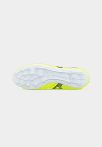 Κάτω όψη ενός ποδοσφαιρικού παπουτσιού νέον κίτρινου χρώματος με λευκή σόλα που διαθέτει πολλαπλές στρογγυλές προεξοχές για πρόσφυση.