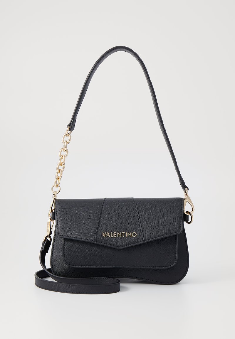 Black leather handbag with a flap design, logo in gold, detachable chain strap, and smooth texture. Features straight and angled lines.