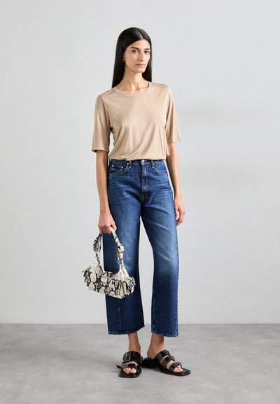 Lichtbeige kortmouwtop met een relaxte pasvorm, gecombineerd met donkerblauwe rechte jeans. Houdt een kleine, textuurrijke tas met zwart-wit slangenprint vast.