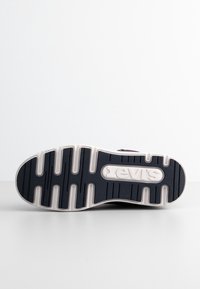Semelle d'une basket Levi's noire et blanche avec une surface antidérapante texturée et le logo Levi's embossé au centre.