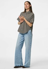 Camicia a maniche corte a righe bianca e nera, abbinata a jeans a vita alta blu chiaro con gamba larga. Scarpe flat completano il look.