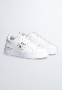 Sneakers in pelle bianca con superficie texture, caratterizzati da borchie metalliche, un logo nero e una suola bianca spessa. Design liscio e lucido.