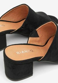 Black suede heeled mules with a block heel, v-shaped opening, and tan insole featuring the brand name "BIANCO." Textured exterior.