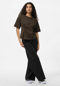 Brūns īsām piedurknēm tops ar brīvu piegriezumu un plecu detaļām, apvienots ar augstu jostasvietu melnām platām biksēm un melnajām sporta apaviem.