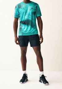 Camiseta deportiva con estampado turquesa y detalles en negro, combinada con pantalones cortos negros y zapatillas negras. Presenta mangas cortas y cuello redondo.