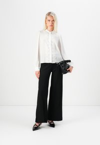Blusa bianca con dettagli in pizzo, maniche lunghe; abbinata a pantaloni neri larghi e a una borsa nera con cordoncino. Completata da decolleté neri lucidi.