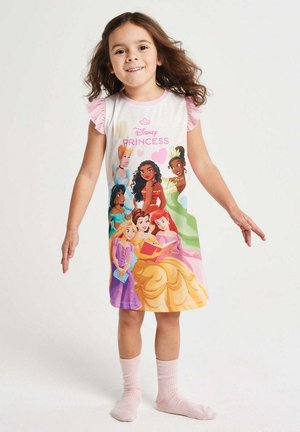 Junges Mädchen lächelt, steht mit leicht ausgebreiteten Armen, trägt ein weißes Kleid mit pinkfarbenen Ärmeln, auf denen Disney-Prinzessinnen abgebildet sind.