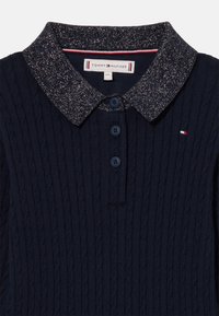 Polo din tricot de culoare albastru marin, cu un design texturat în cablu, guler strălucitor, trei butoane și un accent mic cu logo pe piept.