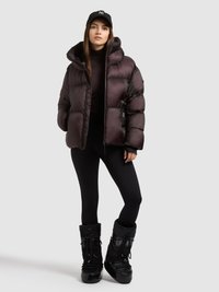 Puffer jacket in dark purple, with a hood and shiny, quilted texture. Paired with black leggings and knee-high, waterproof boots.