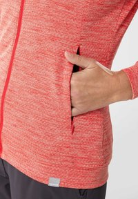 Giacca zip-up rossa con texture, dotata di una tasca laterale, con una zip visibile e un'etichetta del marchio all'orlo. Tessuto liscio con un pattern melangiato.