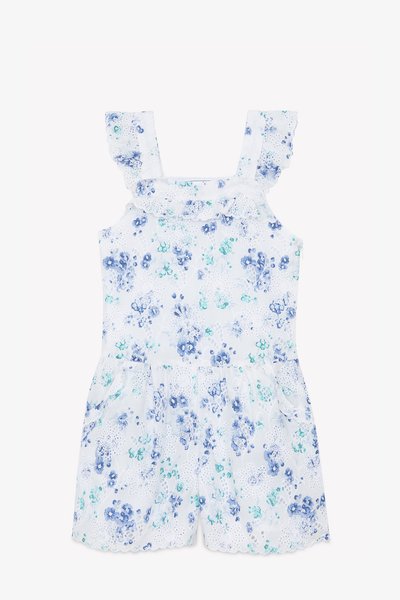 Une combinaison à motif floral blanc avec des fleurs bleues et vertes. Présente des bretelles froncées et un ourlet festonné. Fabriquée en tissu léger.