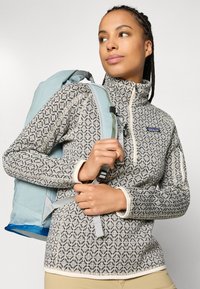 Fleece pullover in crème- en grijsgebroken breisel met hoge kraag. Lichte blauwe rugzak met grijze banden, gaasaccenten en een ritsvak.
