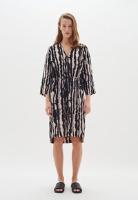 Robe rayée noire et beige avec un décolleté en V, des manches longues et une taille ajustable à lien. Fente à l'ourlet pour faciliter les mouvements.