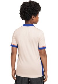 Polo in beige con colletto blu, accenti sulle maniche rossi e blu, e tessuto testurizzato. La vista da dietro mostra maniche corte e dettagli a contrasto.