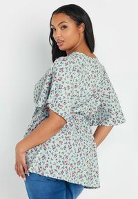 Blusa floreale azzurro chiaro con maniche corte e svasate, decorata con piccoli fiori rosa e blu e con vita arricciata, abbinata a jeans blu.
