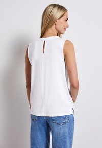 White sleeveless top with a keyhole back detail, made of soft fabric. Features a relaxed fit and side slits for added comfort.