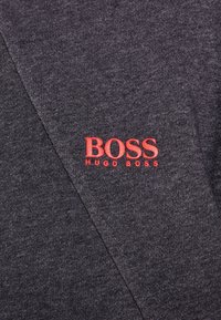 Tessuto grigio scuro con logo ricamato in rosso "BOSS HUGO BOSS" su un indumento piegato.