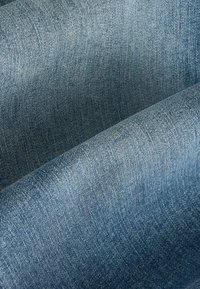 Denimová látka v odstínech od světlé po středně modrou, s texturovaným vazebním vzorem, viditelnými detaily šití a hladkým povrchem.