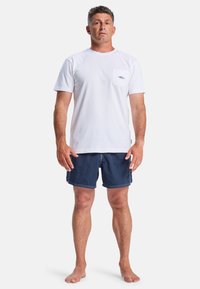 White cotton t-shirt with a pocket and logo, paired with dark blue swim shorts featuring white stitching and a relaxed fit.