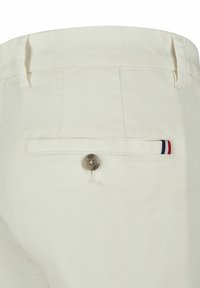 Crème kleurige broek met een achterzak met knoopsluiting. Inclusief merkimpressie en een kleine gestreepte accent in rood, wit en blauw.