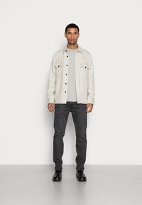 Grijze wolmix hemdjasje met twee borstzakken, knoopsluiting, gelaagd over een grijs T-shirt, gecombineerd met donkere jeans en zwarte laarzen.