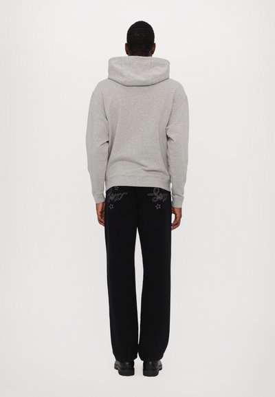 Felpa grigia con cappuccio e polsini a coste, abbinata a pantaloni neri con design ricamati e motivi a stella, vista da dietro.