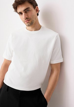 Witte korte-sleeve shirt met een gestructureerd, gebreid patroon. Ronde halslijn en ribbelmanchetten, gecombineerd met zwarte broek.