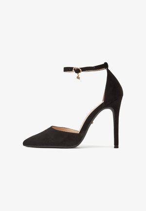 Scarpa con tacco alto in camoscio nero con punta appuntita, cinturino alla caviglia con charm in metallo color oro e sottile tacco a spillo.