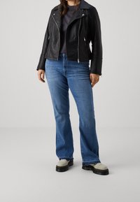 Giacca in pelle nera da moto, jeans a zampa d'elefante blu e scarpe chunky di colore chiaro. Linee pulite, texture liscia e dettagli in hardware argentato.
