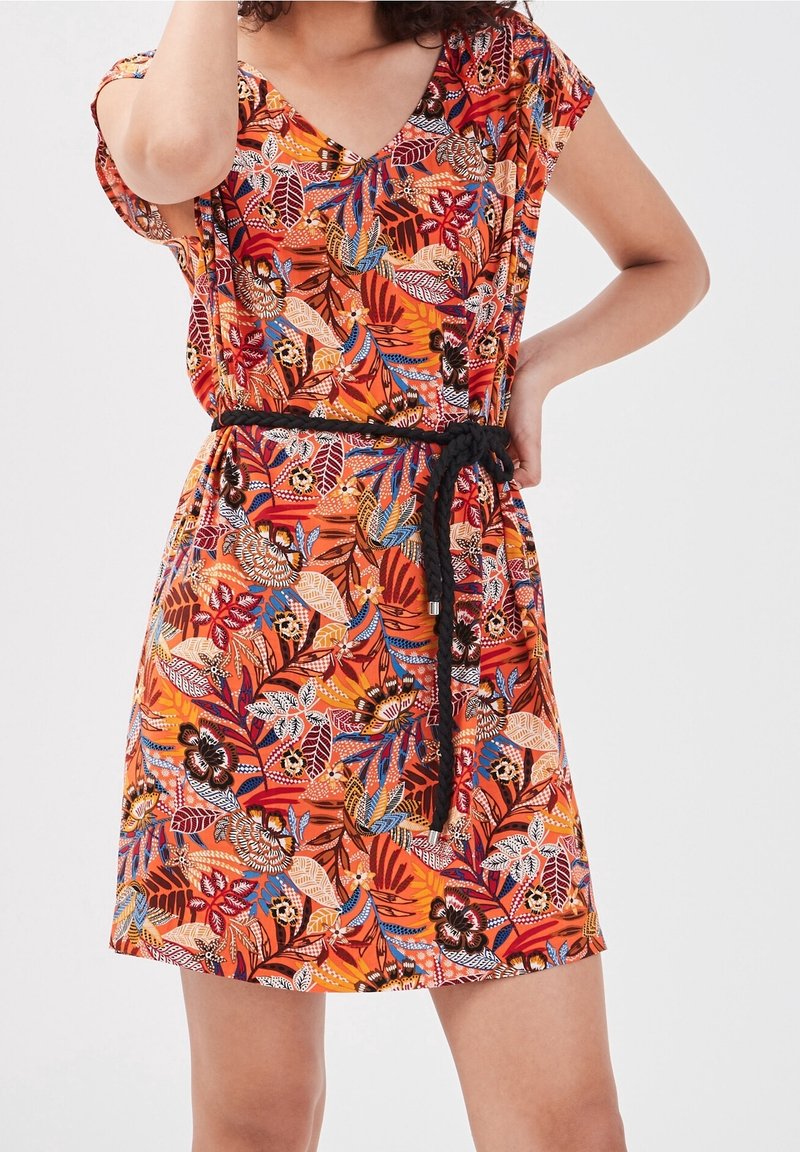 Femme portant une robe à manches courtes avec un motif floral et feuilles orange, rouge et bleu, et une ceinture tressée noire à la taille.