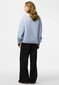 Pull tricoté bleu clair texturé à manches longues assorti à un pantalon large noir à fines rayures. Le pull a une coupe décontractée et des poignets côtelés.