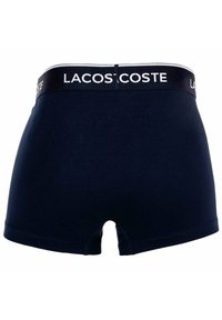 Boxer da uomo blu navy con elastico nero, caratterizzati dal logo bianco "LACOSTE", mostrati da dietro.