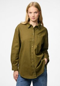Olivgrön knappad skjorta med spetsig krage, en bröstficka och avslappnad passform. Tillverkad av ett mjukt, strukturerat tyg.