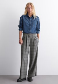 Denim skjorte med knapper, lange ærmer, brystlomme, parret med grå ternede vidde bukser og kraftige sorte plateau sko.
