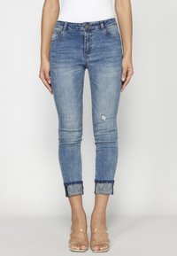 Smala jeans i blekt blå denim med knapp i midjan, lätt slitage och uppvikt fåll som visar ett mönstrat innerfoder. Klar, slät textur.