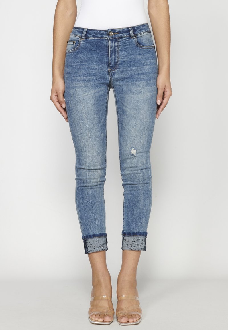 Smala jeans i blekt blå denim med knapp i midjan, lätt slitage och uppvikt fåll som visar ett mönstrat innerfoder. Klar, slät textur.
