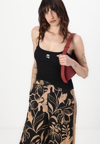 Čierny rebrovaný top bez rukávov s malou bielou grafikou, v kombinácii s béžovými nohavicami s kvetinovým vzorom a červenou crossbody taškou.
