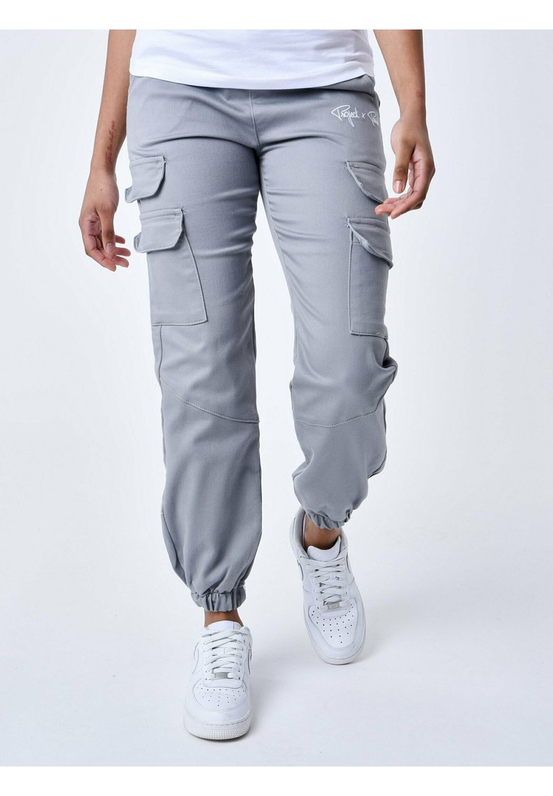 Grijze cargobroek met meerdere zijzakken, elastische boorden en een gladde textuur. Gecombineerd met witte sneakers voor een casual look.