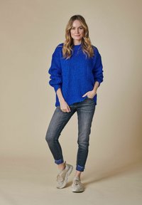 Helle blaue, grob gestrickte Pullover mit übergroßen �Ärmeln, kombiniert mit dunklen Jeans und beigen Sneakers. Schlichtes, strukturiertes Design.