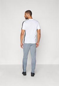 Witte sportieve t-shirt met korte mouwen en zwarte zijaccenten, gecombineerd met grijze taps toelopende joggers met zwarte panelen langs de zijkanten.
