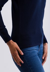 Tmavě modrý svetr s dlouhým rukávem vyrobený z měkké látky, přiléhavý design, hladká textura, spárovaný se světle modrými džíny.