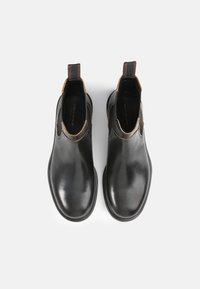 Botas de tobillo de cuero negro con un acabado suave, que presentan paneles laterales elásticos y costuras en marrón en contraste a lo largo de las costuras.