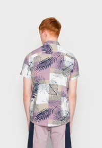 Takahimik na likurang bahagi ng kamiseta na may maiikli ang manggas at butones. Naglalaman ito ng timpla ng lila, puti, at beige na may tropical leaf pattern at checkered na disenyo.
